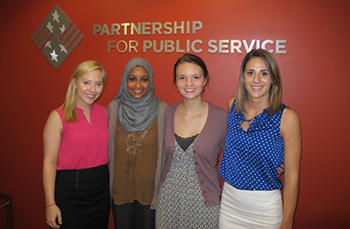Four Partnership for Public Service Interns stand in front of a wall with a Partnership for Public Policy sign on it.