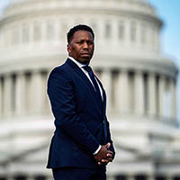 A man in a suit stands in front of the Capitol Building.