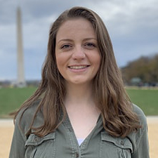 Katherine Truitt, Government and International Politics major, stands in a green shirt in Washington, DC with the Washington Monument in the background.