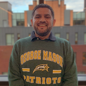 Ernesto Galeas stands in front of a window while wearing a George Mason University sweatshirt.