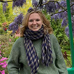 A woman in a green sweater and a scarf stands outside while smiling