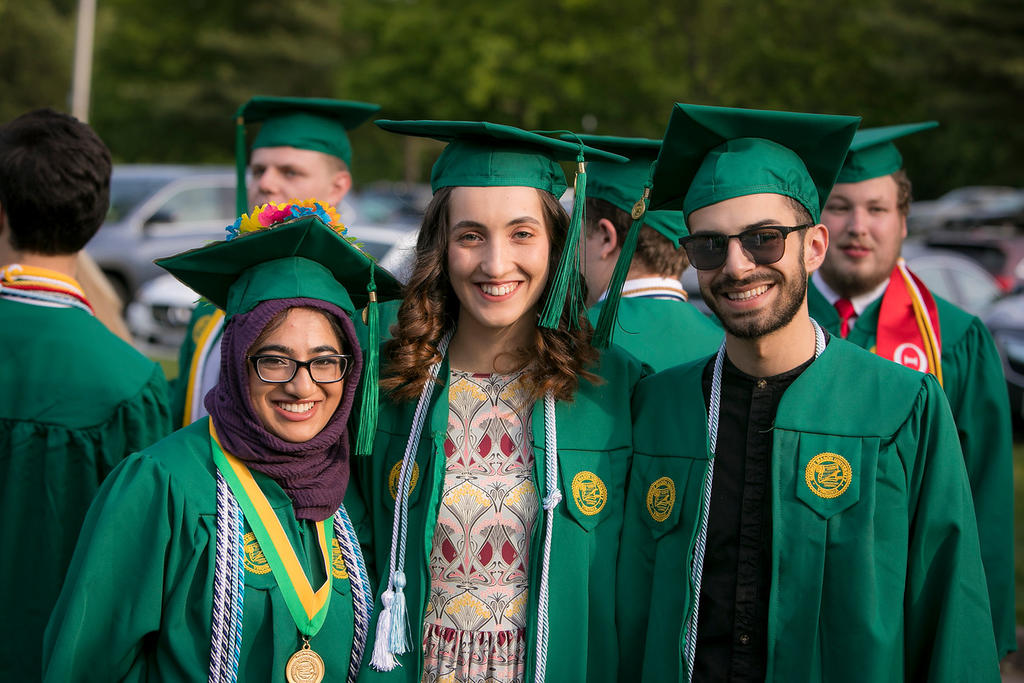 Three Schar School students standing together in a gown and cap for graduation