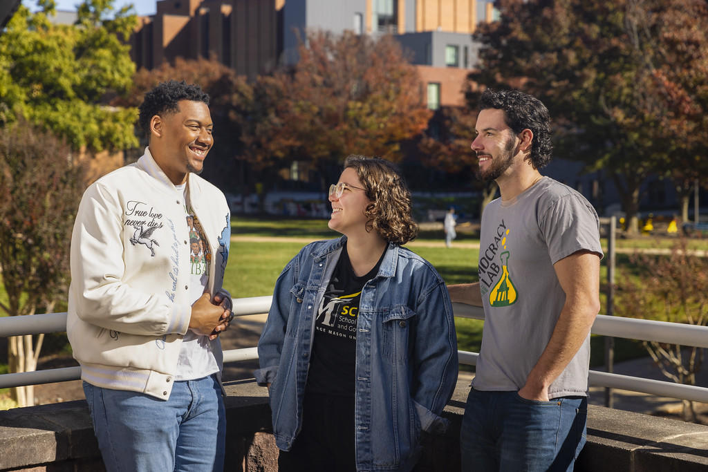 Three students talking to one another and smiling in front of campus