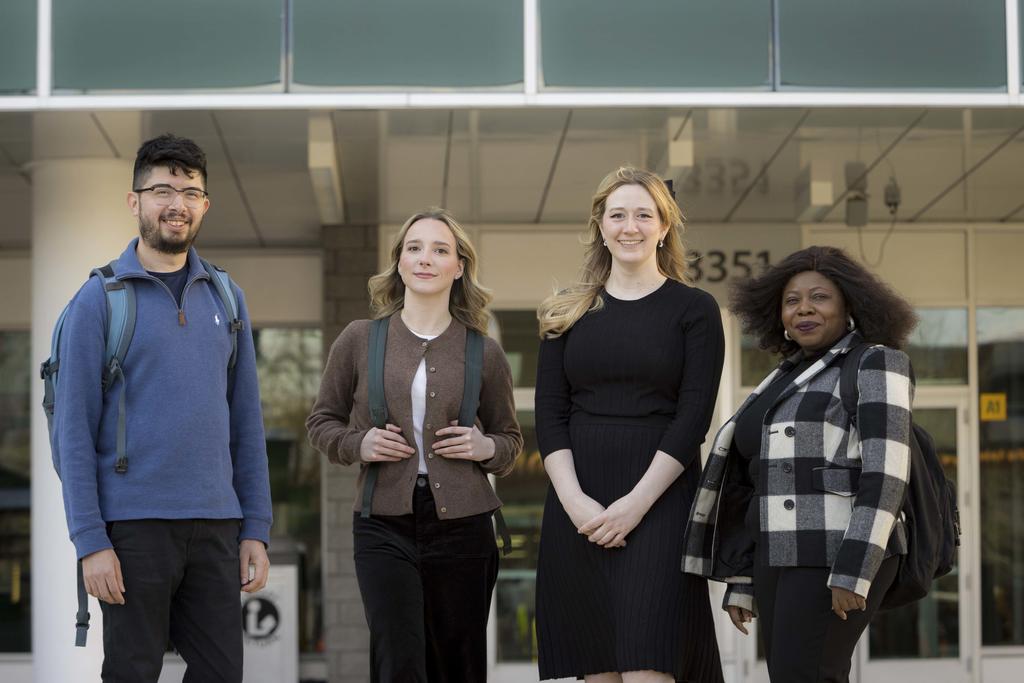 Four students standing together in front of a building and smiling