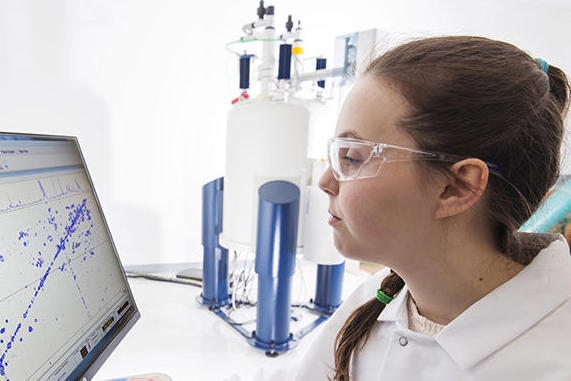 A woman in a white lab coat sits at a desk while working on a computer
