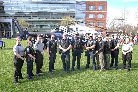 A group of police officers stand in front of a Fairfax County police helicopter