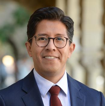 A man with dark hair and eyeglasses smiles at the camera.