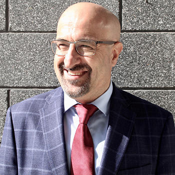 A close up of a bald man in eye glasses and a red tie smiling at the camera.