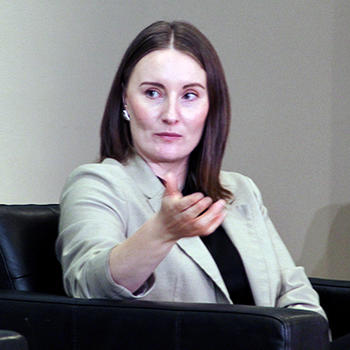 A woman in a brown jacket sits in a black leather chair.