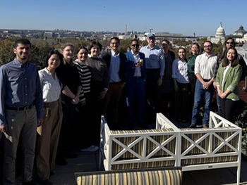 A group of 14 people pose on an outdoor terrace with views of the U.S. Capitol in the distance.