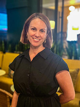 A woman in a dark top with short brown hair smiles at the camera.