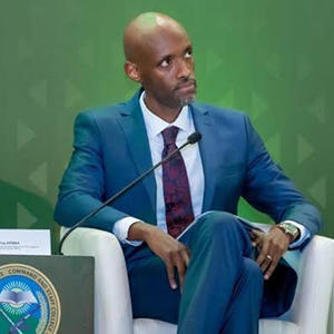 A man in a blue jacket, white shirt, and necktie glances off camera.