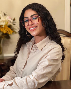 A woman in a cream-colored blouse and wearing eyeglasses smiles at the camera.