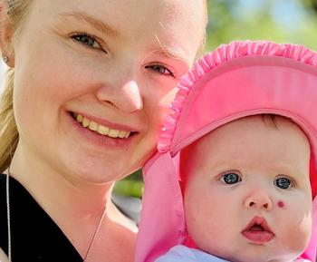 A blond woman holds a baby as both look at the camera.
