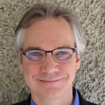 A man with salt and pepper hair and eyeglasses smiles at the camera.