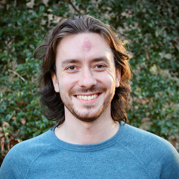 A man with long dark hair in a blue shirt smiles at the camera.