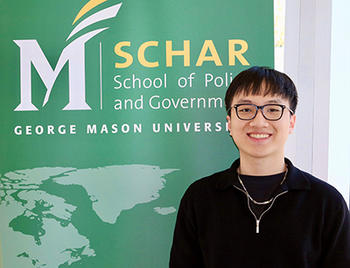 A man in a black sweater stands in front of a green and gold sign.