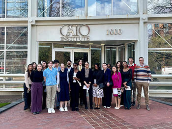 A group of well-dressed people stand in front of a glass and chrome building.