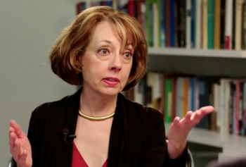 A woman in a dark top gestures off camera.